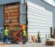 Contractor repairing damaged siding panels on a commercial building exterior