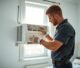 HVAC technician fitting a window AC heat pump into a residential window during installation.